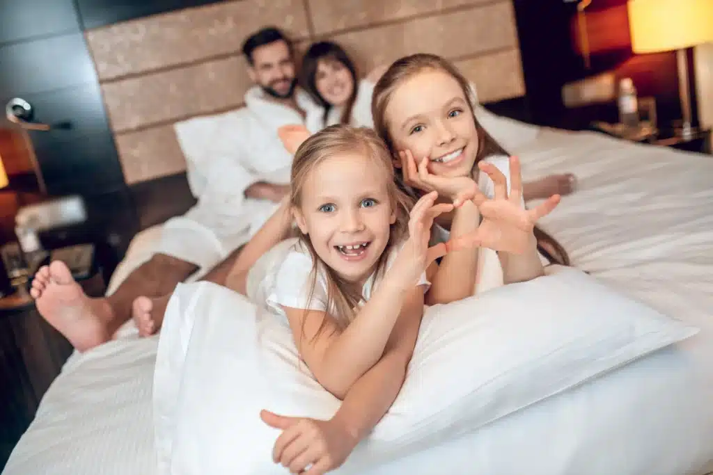 Šťastná rodina s deťmi odpočíva na posteli v hoteli počas kúpeľného pobytu.
